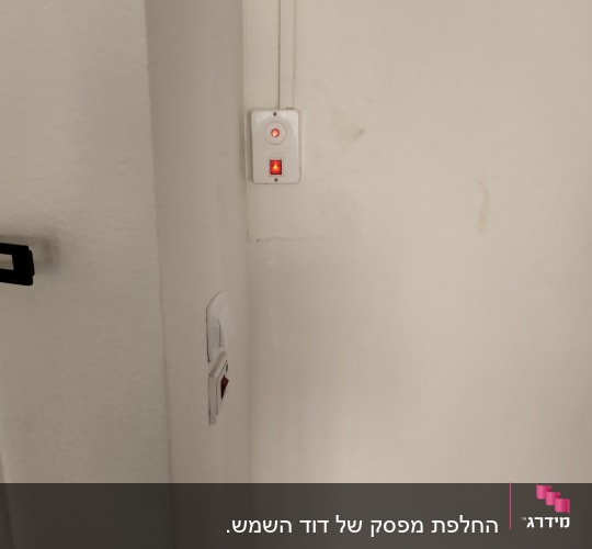 מתג דולק עם נורית חיווי אדומה על קיר לבן
